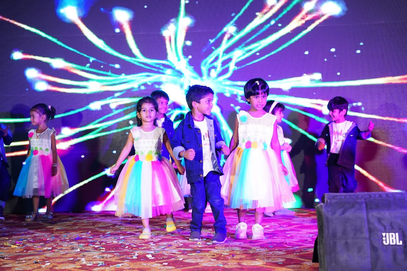 Little Ville students in rainbow costumes dancing on stage at Annual Day 2025-26