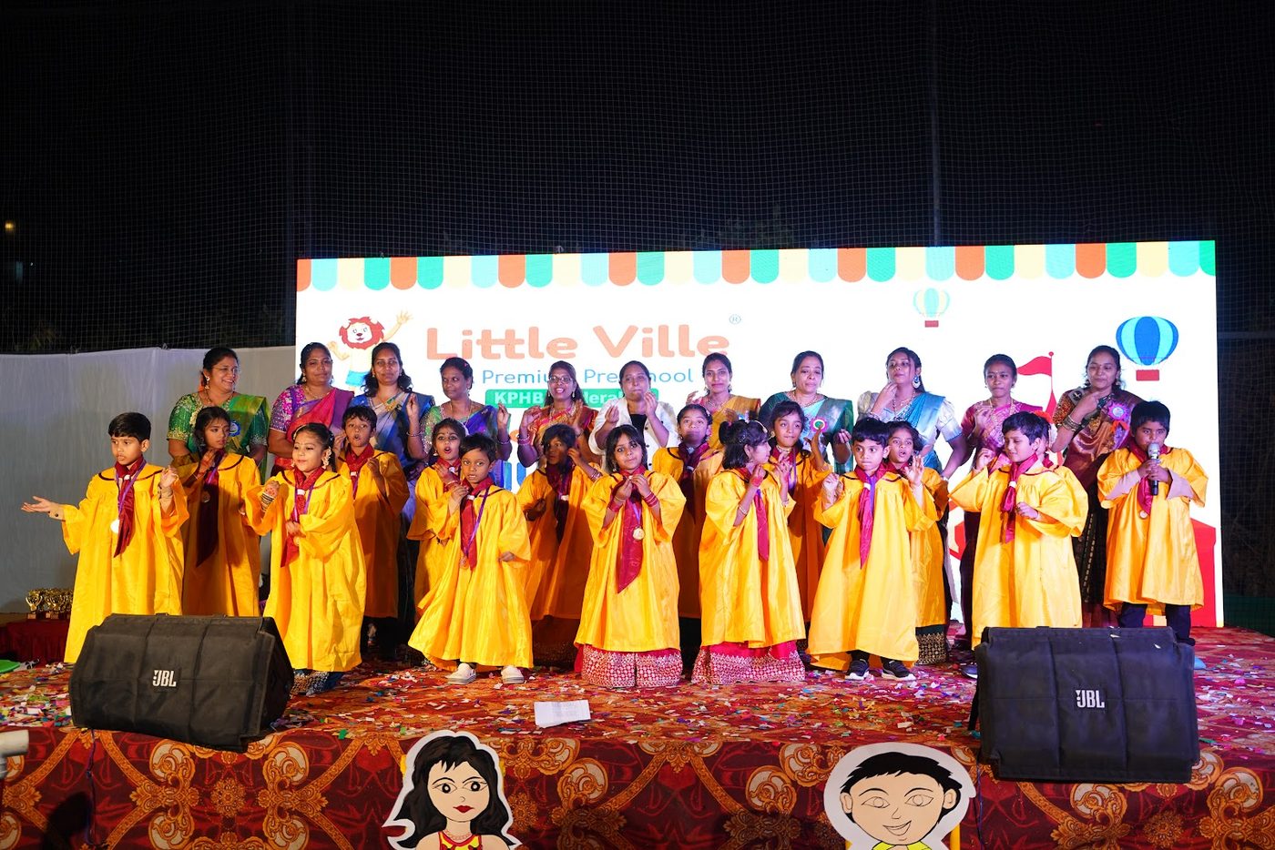 Little Ville graduates singing together on stage in their gowns at Grad Day