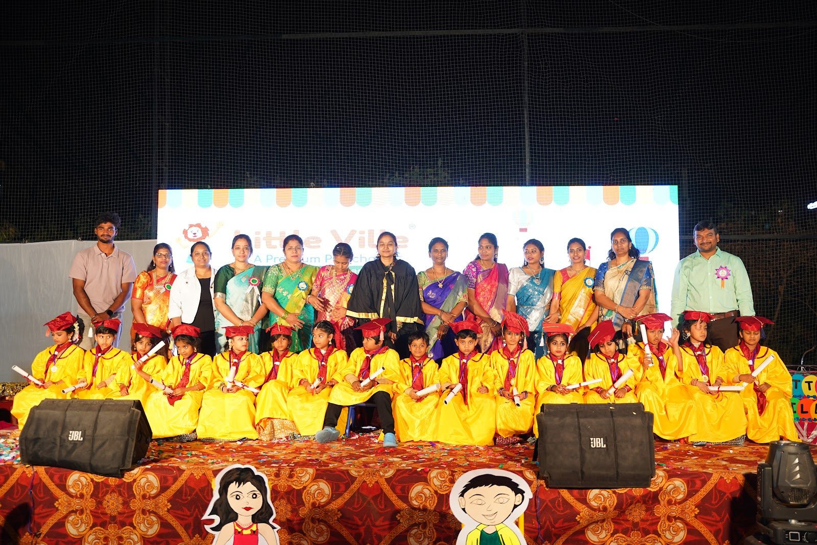 The Little Ville graduating class of 2025-26 on stage in caps and gowns with their teachers