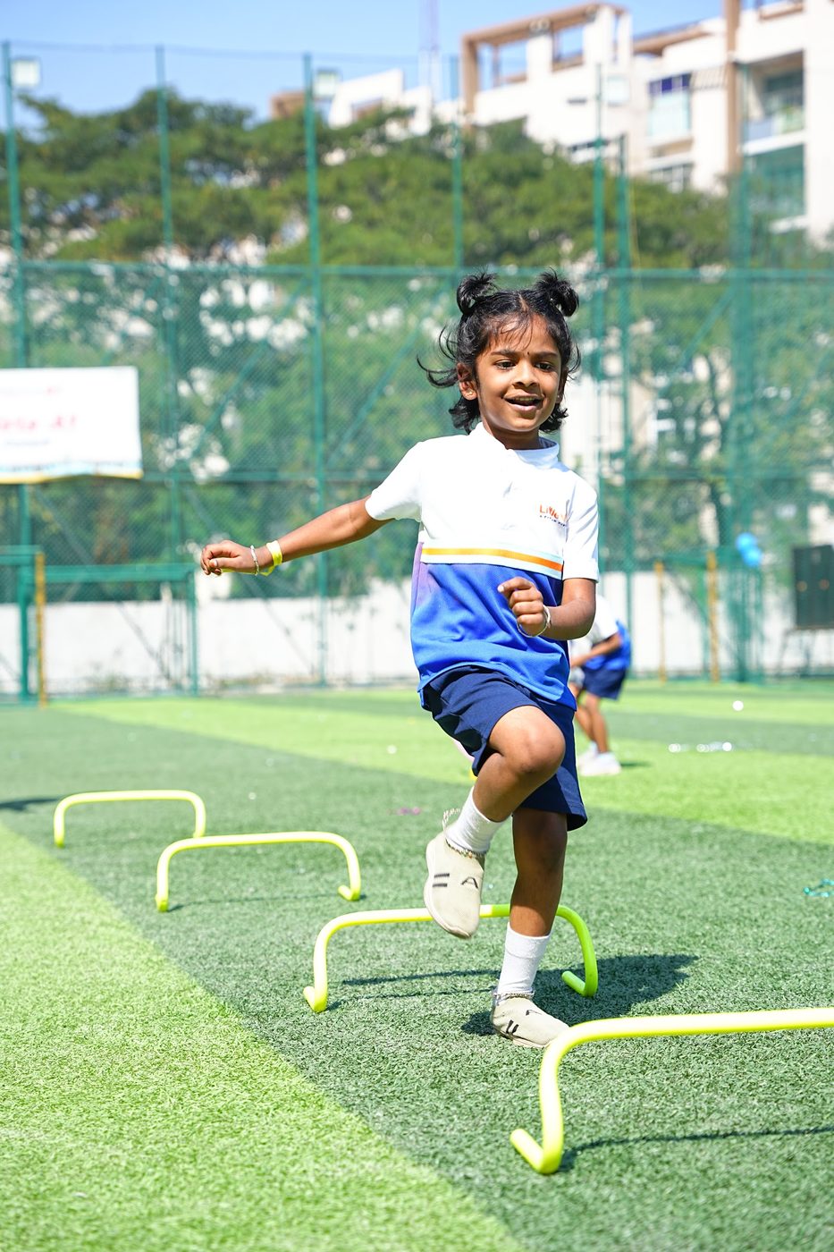 A Little Ville student mid-jump over a hurdle on the field at Khel Utsav Sports Day 2025-26
